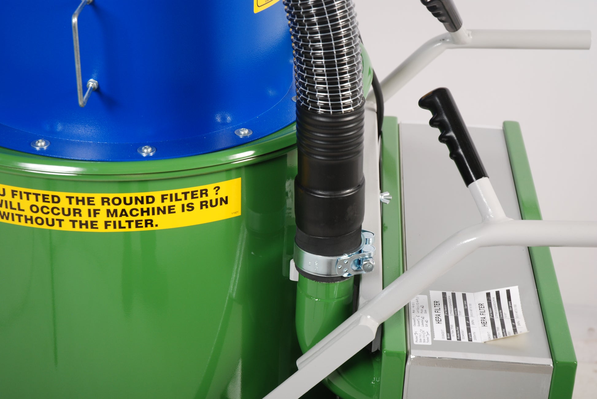 Green machine with blue top and black hose, featuring a warning label.